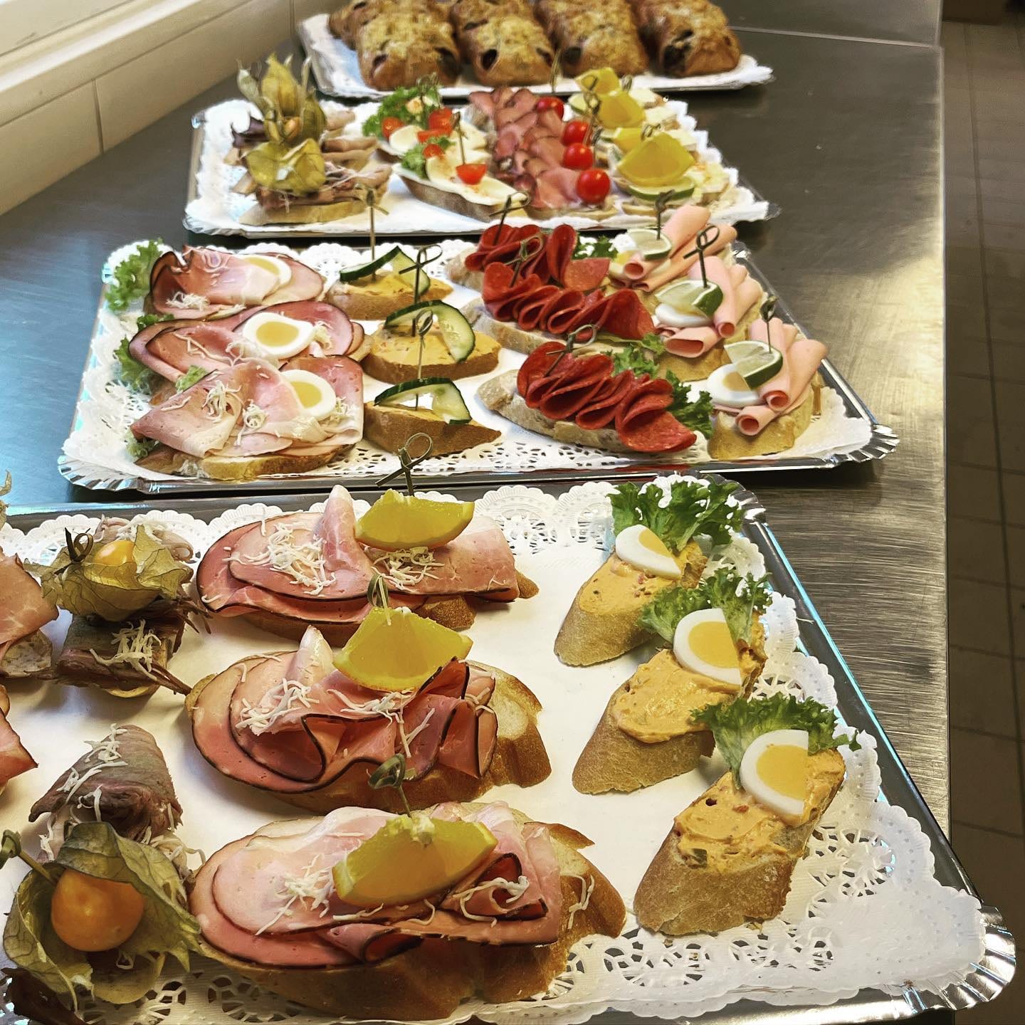 Mehrere Cateringplatten mit garnierten Brötchen und Mohntaschen auf einer Arbeitsfläche