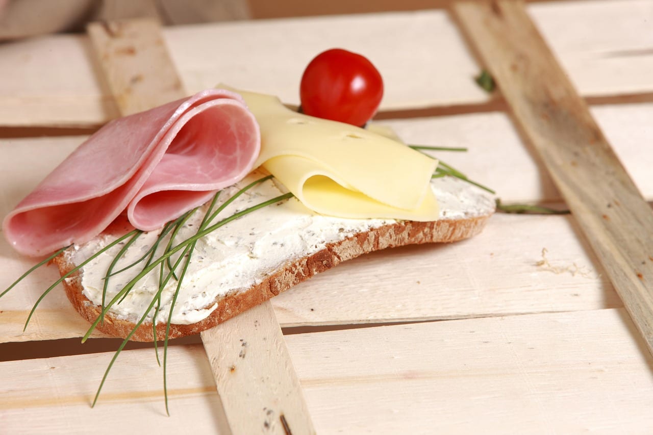 Belegtes Brot mit Frischkäse, Schinken, Käse und Schnittlauch auf einem Holzbrett